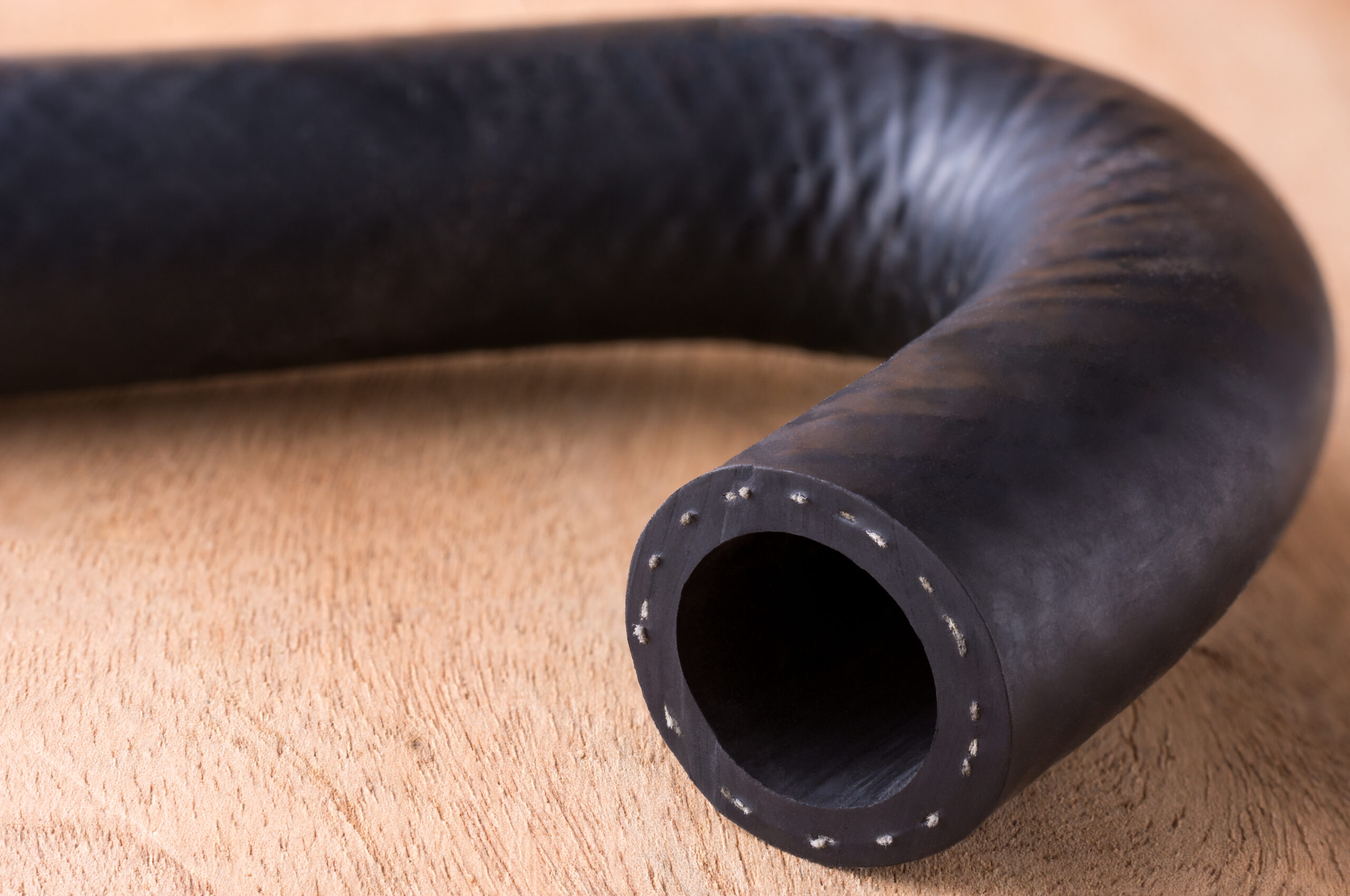 automotive hose, fluid carrying engine hose made of reinforced synthetic rubber on a wooden table top, closeup macro with copy space